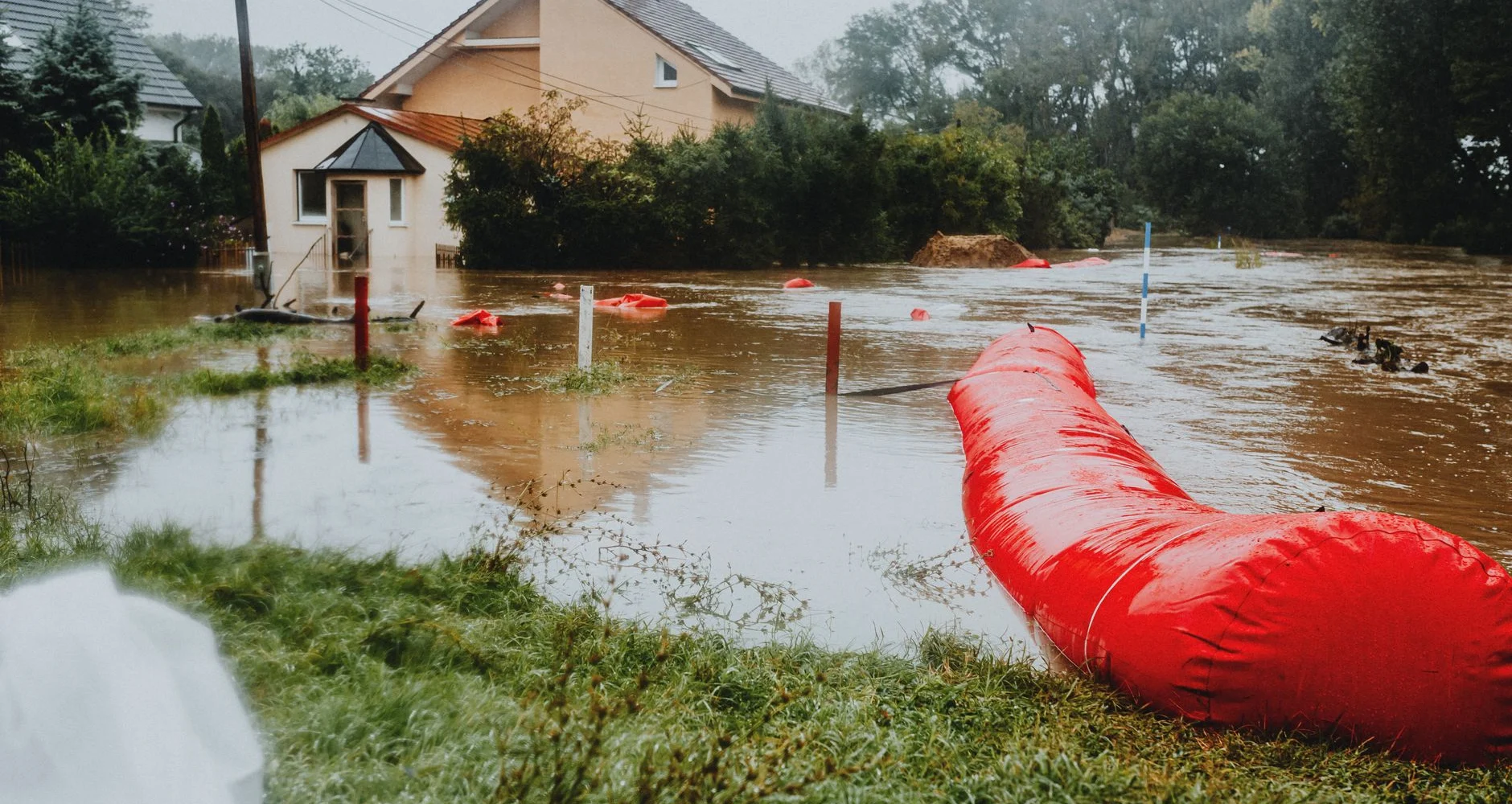 Flooded yard and home with a red flood barrier