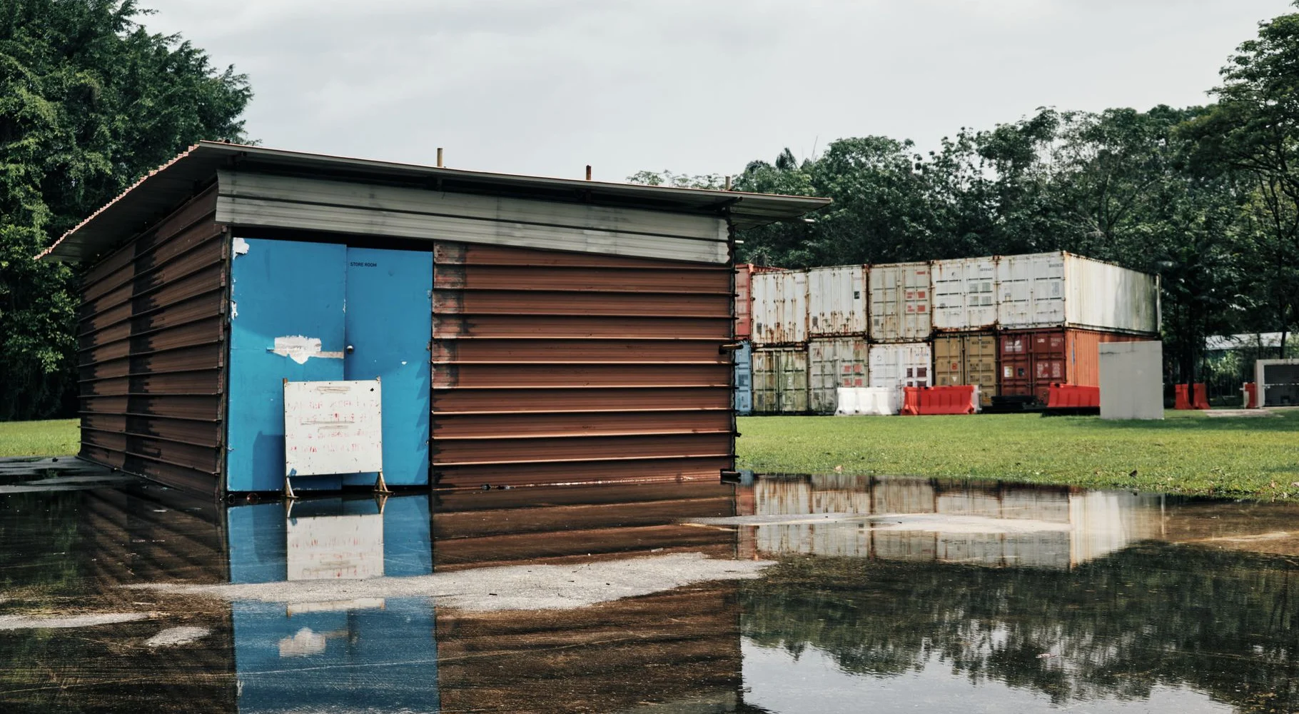 Floodwater around a building and shipping containers on an overcast day