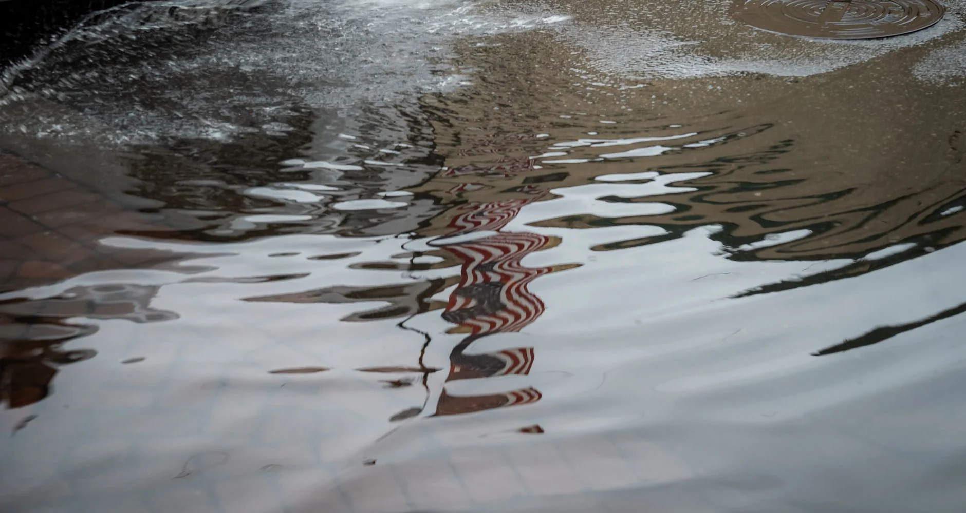Rainwater flooding a city street near a storm drain