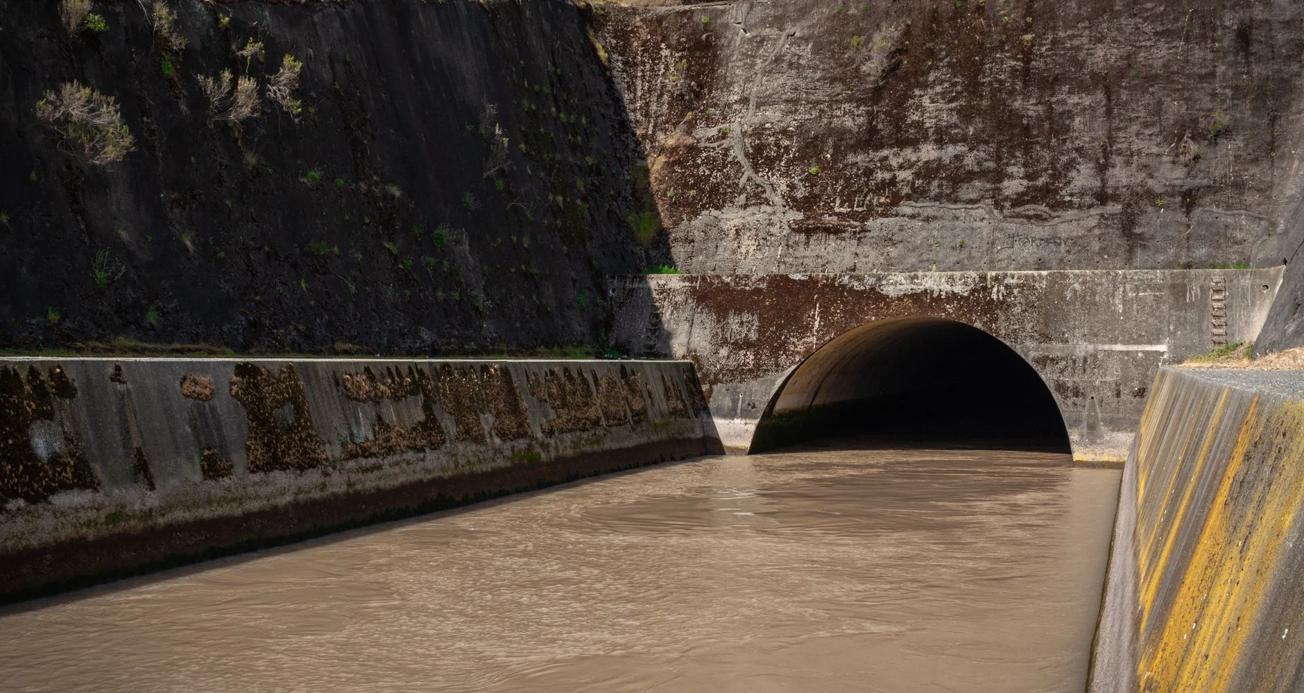 Concrete storm drain culvert with water flowing into a tunnel